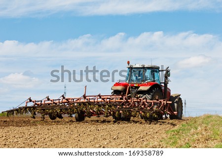 Farmer plowing the field. Cultivating tractor in the field. Red farm tractor with a plow in a farm field. Tractor and Plow