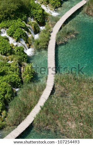 Wooden boardwalk passage in Plitvice National Park. Aerial view. Vivid turquoise lake.