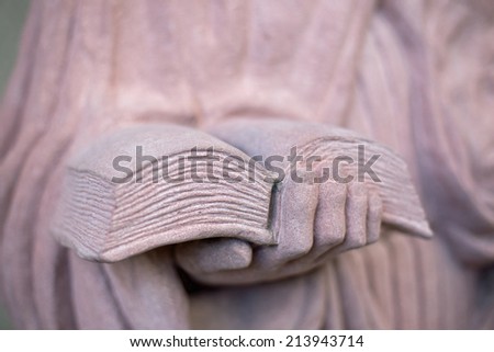A hand holding a book, statue of stone