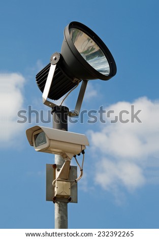 Surveillance camera with floodlight, blue cloudy sky