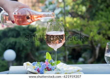 Waiter pouring a glass of cold rose wine, outdoor terrace, sunny day, green garden background