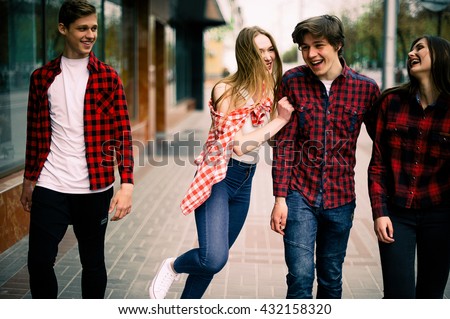 Four happy trendy teenage friends walking in the city, talking each other and smiling. Lifestyle, friendship and urban life concepts.