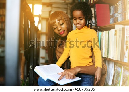 African mother and daughter reading together in library. Focus on little girl.