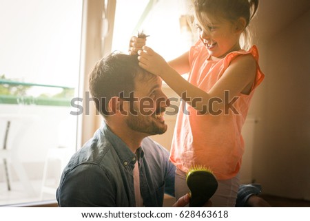 Father and daughter plying at home together. Girl is playing with her dad and says his hairstyle.