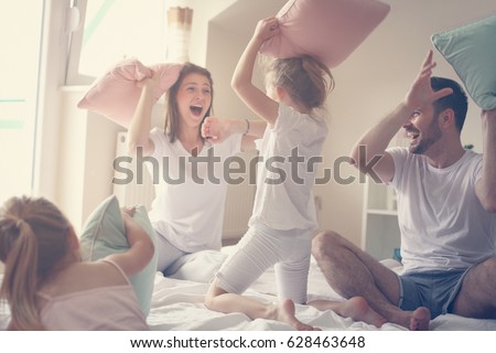 Family having funny pillow fight on bed. Parents spending free time with their daughters.
