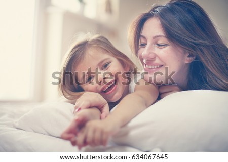 Mother with her cute little daughter lying on bed. 
Enjoy together in free time. Looking at camera.