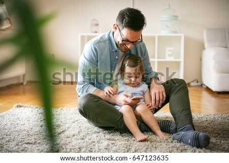 Single father wit his daughter using smart phone. Father and little baby watching something funny at smart phone.