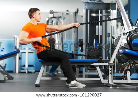 Smiling athlete bodybuilder man doing muscles exercises at weight machine in fitness sport club gym