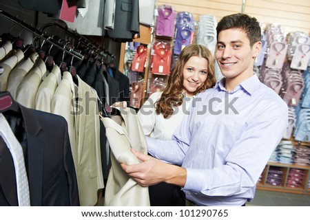 Young man and woman choosing suit jacket during apparel shopping at clothing store