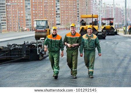 three happy road construction workers walking over asphalt paver machine