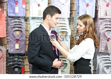 Young man choosing shirt and necktie during apparel shopping at clothing store