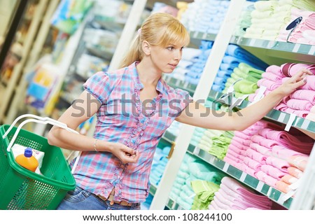 woman with basket choosing towel at household chemistry goods department of shopping mall