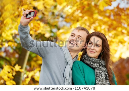 Two Smiling young people taking a picture with mobile phone in autumn park outdoors
