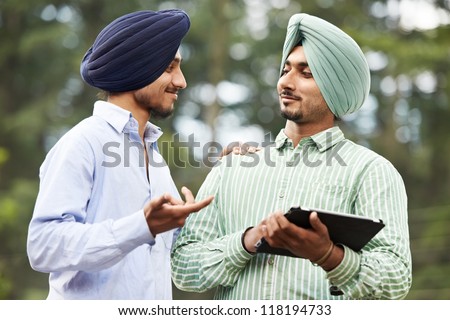 Two smiling authentic native indian punjabi sikh men in turban discussing something with tablet computer
