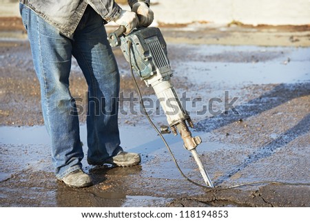 Builder worker with pneumatic hammer drill equipment breaking asphalt at construction road works