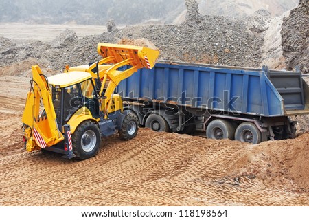 Wheel loader Excavator with backhoe loading sand into dumper truck at eathmoving works in construction site quarry