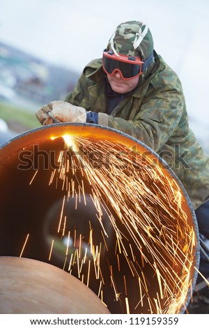 Construction Welder worker in protective glasses cutting metal pipe at building site with welding flame torch cutter