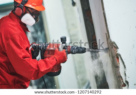 worker with demolition hammer removing plaster or stucco from wall