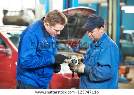 two mechanic engineers examining spare part of internal combustion engine of automobile car at repair service station