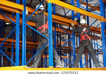 team of two warehouse workers in uniform with power tool drilling hole during rack arrangement erection work