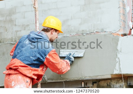 facade work. builder plastering outside wall with putty knife float