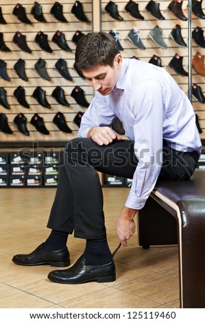 Young man trying on new shoes during footwear shopping at shoe shop
