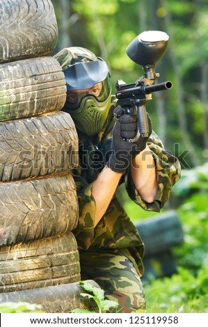 paintball sport player in protective uniform and mask aiming and shooting with gun outdoors
