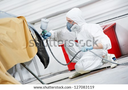 auto mechanic worker painting car bumper at automobile repair and renew service station shop by spraing black color paint