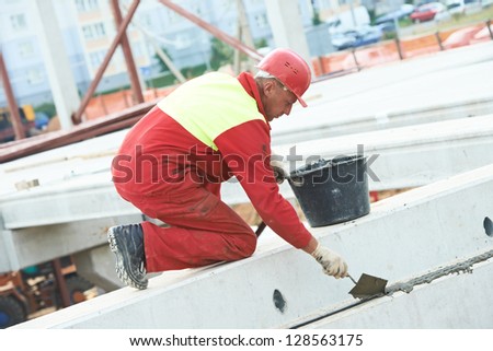 builder worker in safety protective equipment putting cement mortar on concrete floor slab panel at building construction site