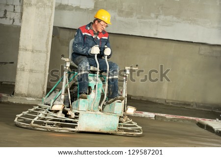Worker trowelling and finishing of concrete by special construction equipment machine