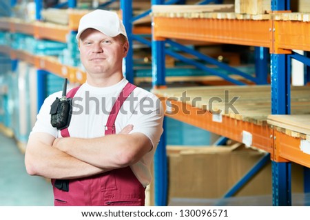 young handsome worker man in uniform in front of warehouse rack arrangement stillages