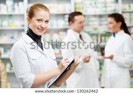 Female happy pharmacist chemist woman standing in pharmacy drugstorewit her colleagues