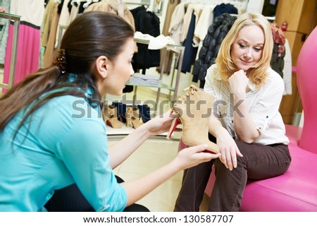 Young woman and assistant choosing footwear during shopping at shoe shop