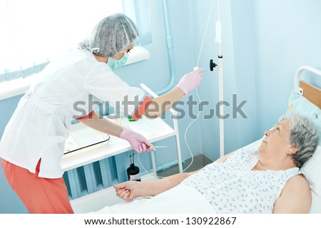 Young nurse doctor in medic uniform preparing dropper for intravenous injection in hospital clinic for elderle woman