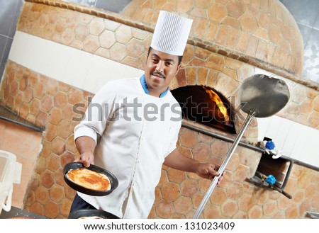 One arab chef baker in white uniform making pizza at hotel restaurant kitchen