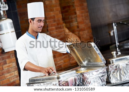 Adult arab chef man in uniform demonstrating food on cooker in resort hotel restaurant kitchen