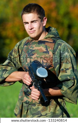 Serious paintball player man in protective camouflage uniform and mask with marker gun outdoors
