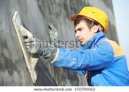Young builder worker at facade plastering work during industrial building with putty knife float