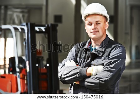 Young Smiling Warehouse Worker Driver In Uniform In Front Of Forklift Stacker Loader