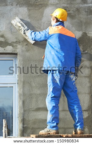 Male builder plastering exterior wall during industrial facade building with putty knife float