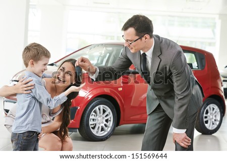 At automobile sales centre. Car salesperson selling new automobile to young family with child boy