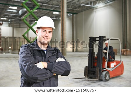 young smiling warehouse worker driver in uniform in front of forklift stacker loader
