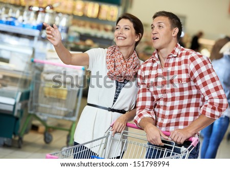 Family couple with trolley cart in meat grocery supermarket during weekly food shopping