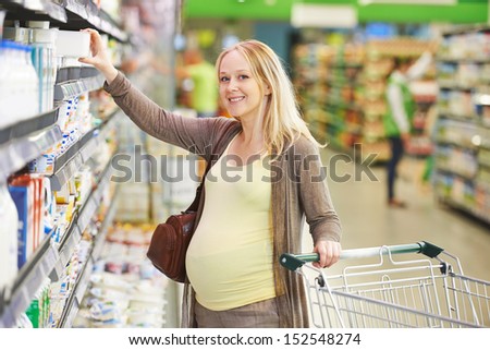 Young Pregnant Woman Choosing Fresh Milk Produces At Shopping In Dairy Supermarket Store