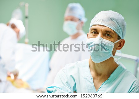 Portrait Of Surgeon Medic In Front Of Surgeons Perfoming Operation On A Patient At Cardiac Surgery Clinic