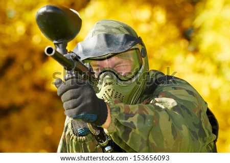 paintball sport player in protective uniform and mask aiming gun before shooting in summer