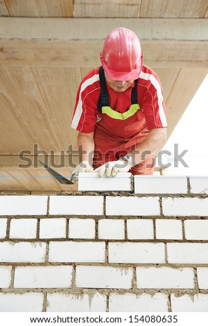 Builder construction mason worker bricklayer installing brick with trowel putty knife outdoors