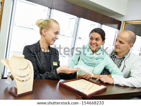Sales assistant in jewelry shop demonstrating bracelet to young couple customer during gift selecting