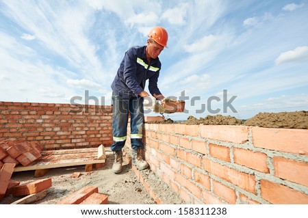 construction mason worker bricklayer installing red brick with trowel putty knife outdoors