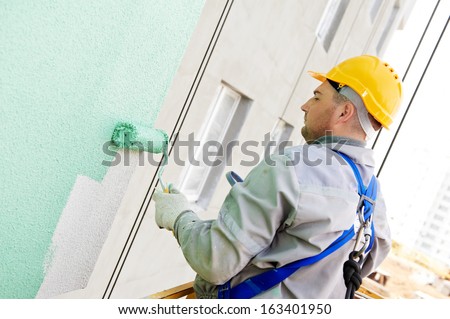 builder worker painting facade of high-rise building with roller